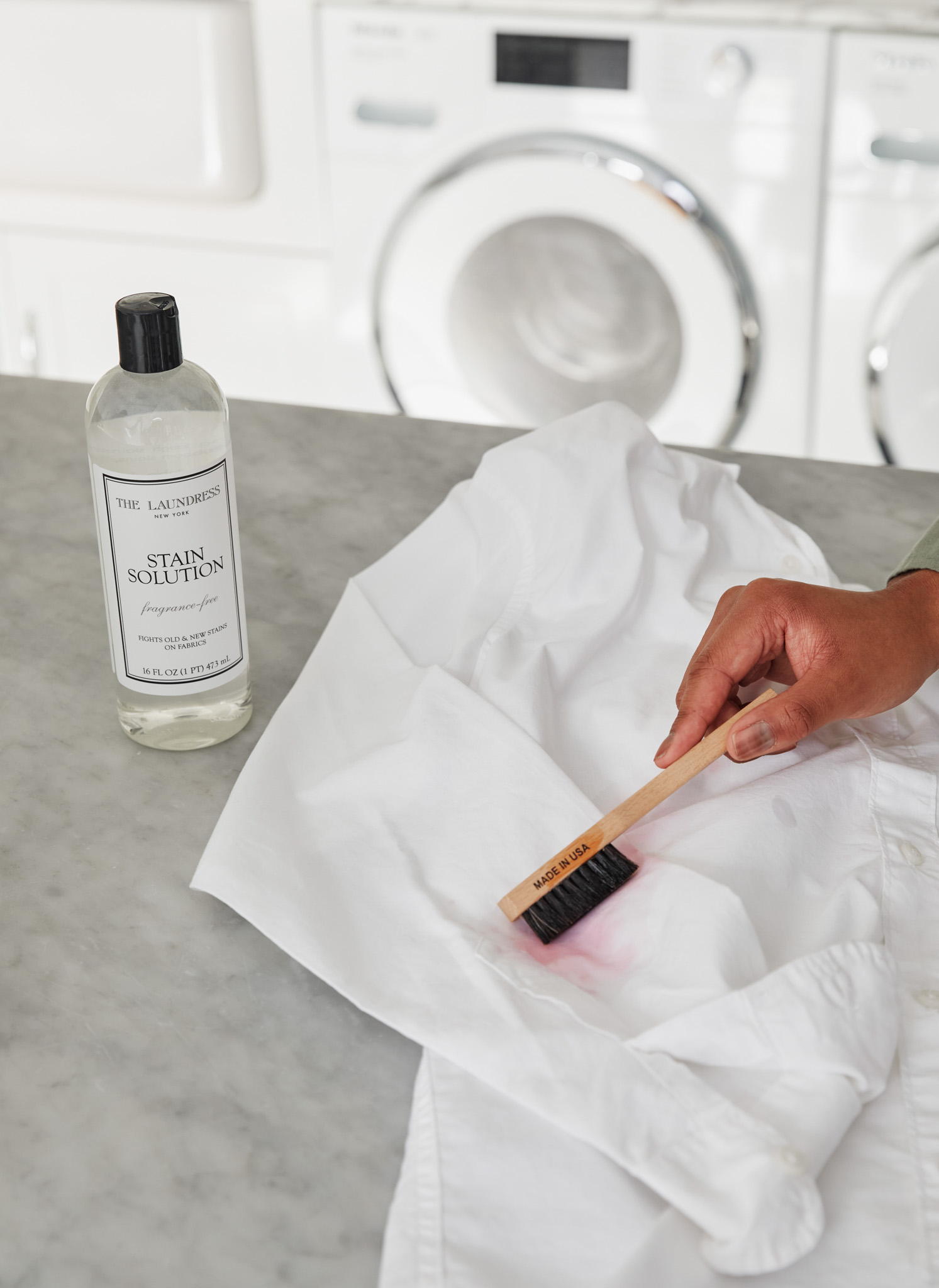 The Laundress Stain Solution and Stain Brush being used to remove a stain from a white sheet. 