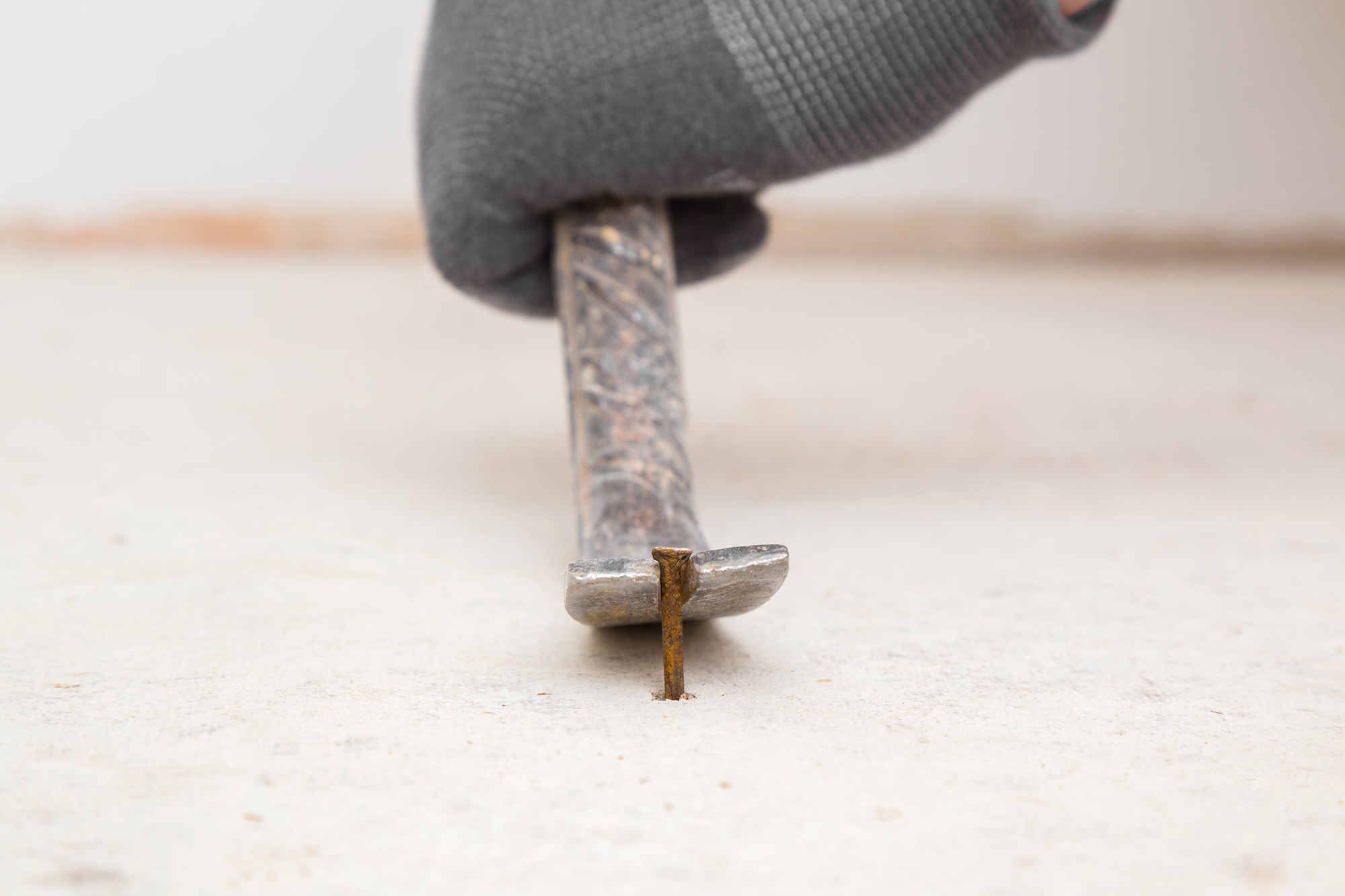 A person wearing work gloves and removing a nail with a prybar.