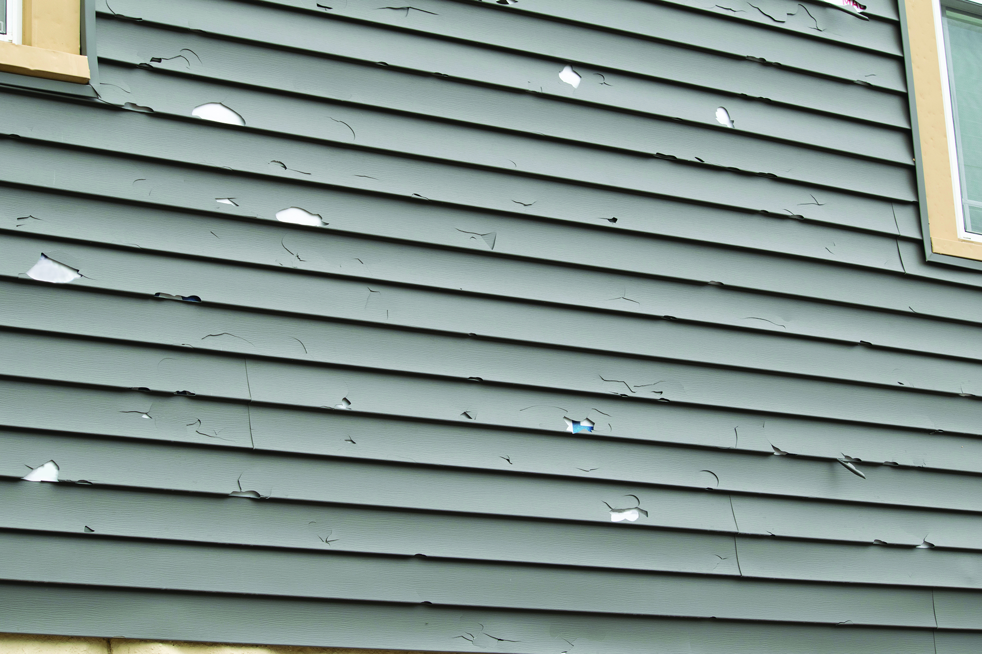 A close-up of a house with old, peeling gray siding.