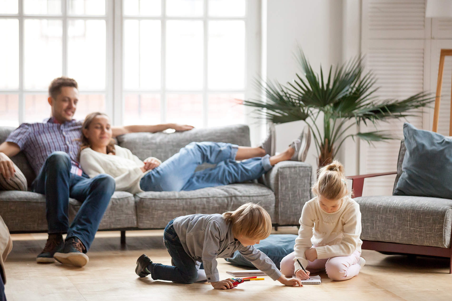 Couple sitting comfortably on a couch in front of insulated windows while two children are drawing on the floor in home