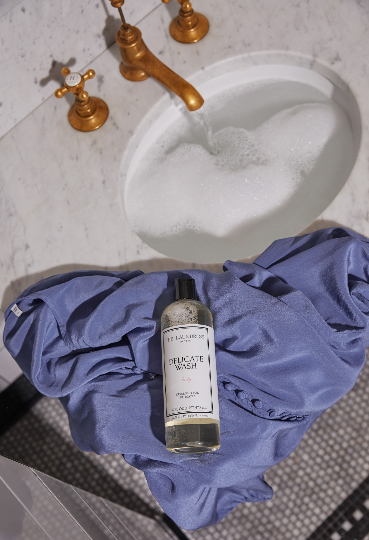 The Laundress Delicate Wash, ideal for vintage garment care, resting on a blue vintage dress. 