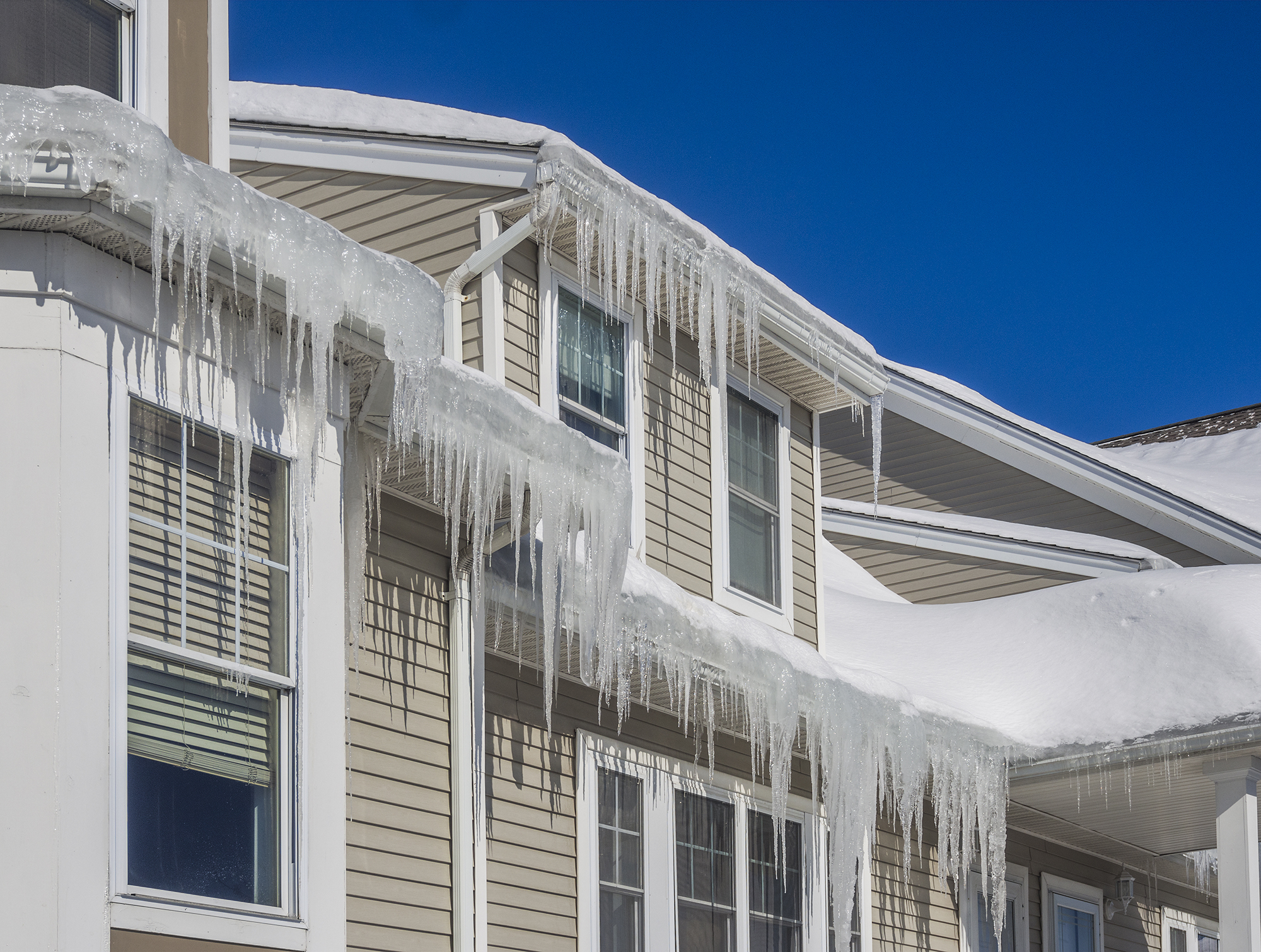 Icicles running along the entire span of the gutters on the back of a home that are hanging down the side of the house.