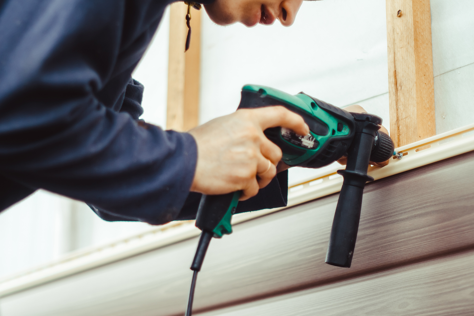 A man installing siding with a drill to a home.