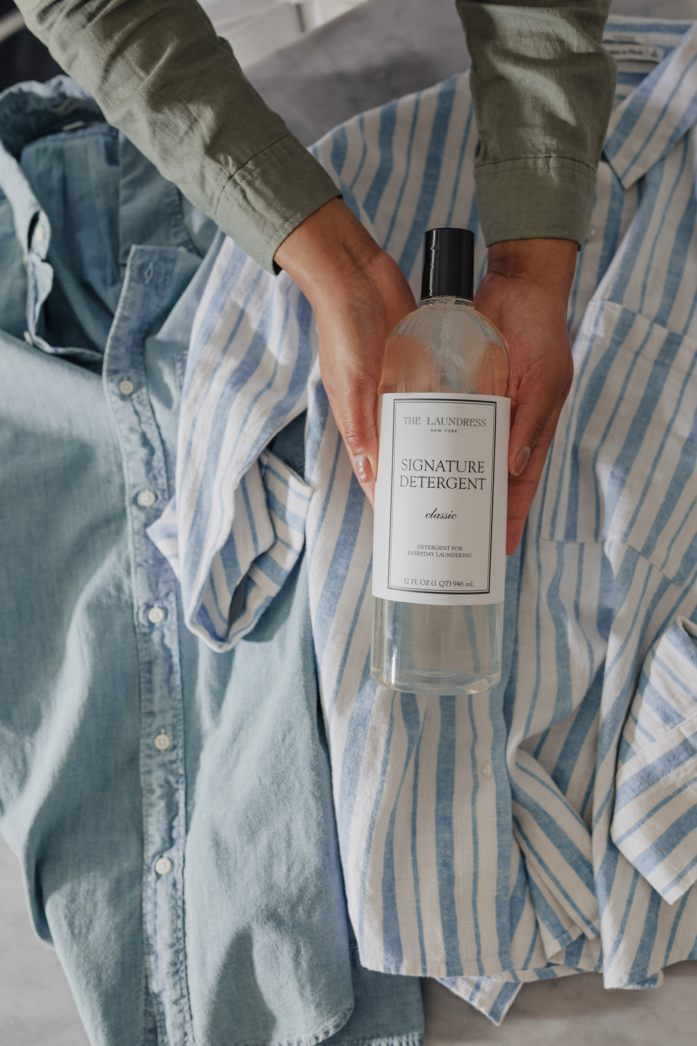 hands holding the laundress signature detergent over a pile of shirts