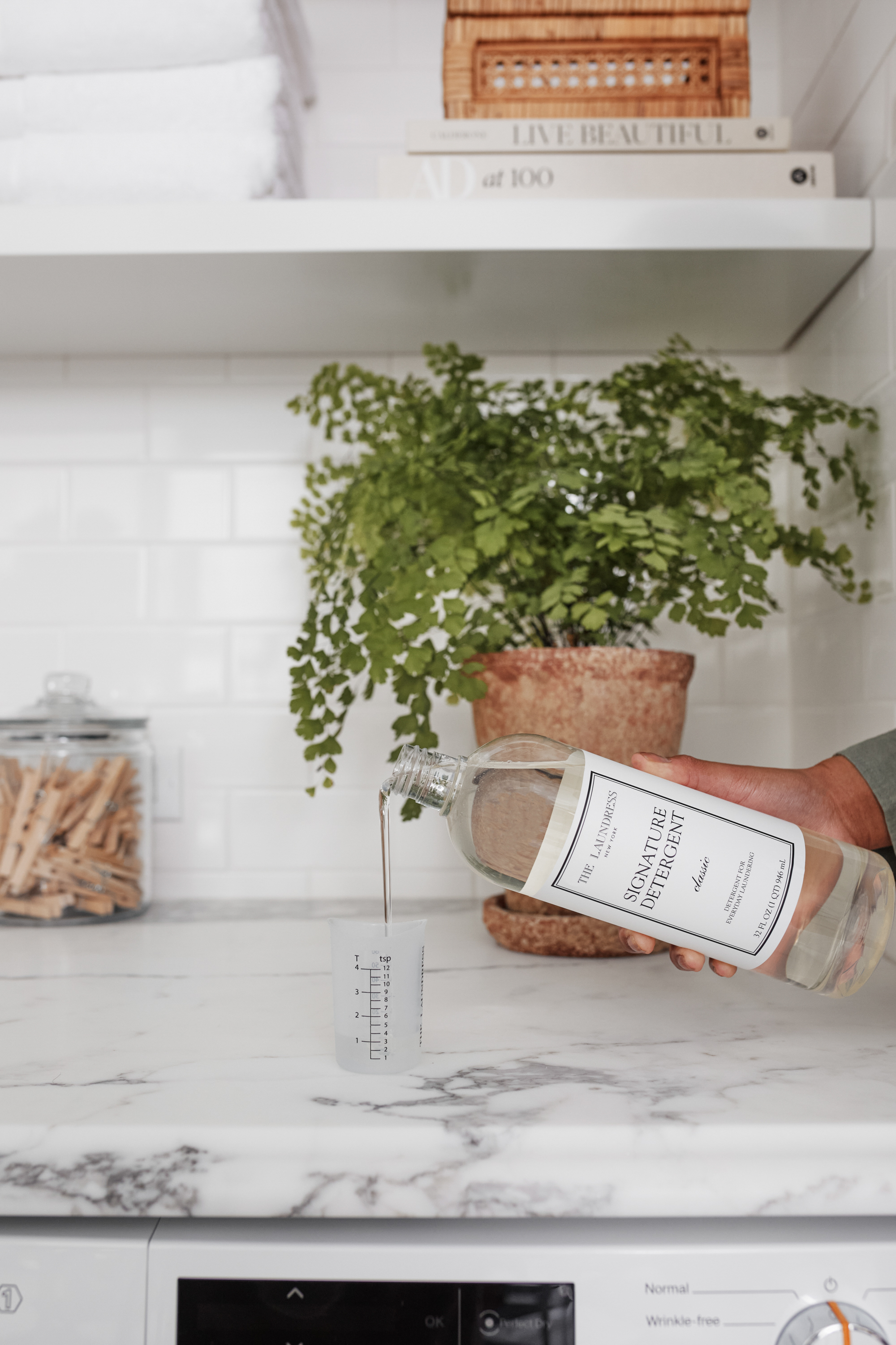 A person pours The Laundress Signature Detergent for everyday laundering into The Laundress Laundry Measuring Cup. 